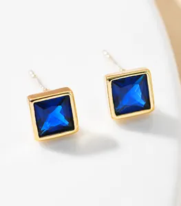 Macro shot of square blue stone earrings with gold finish on white ceramic tray