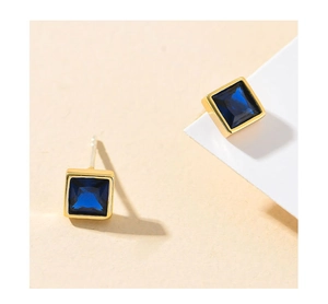 Macro shot of square gold-plated earrings with deep blue crystal inlay on a minimalist stand