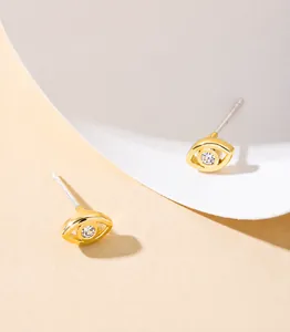 Detailed close-up of golden evil eye earrings with centered clear zircon and silver needles