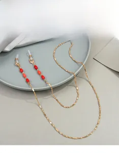 Détail d'une chaîne à lunettes dorée avec perles rouges, fermoir et embouts silicone