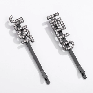 Détail de pinces à cheveux en métal noir avec strass formant les mots just et HELLO
