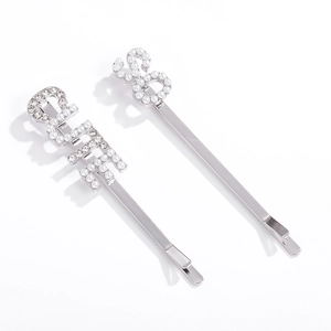 Détail de barrettes argentées avec perles et strass formant les lettres GIRL et S