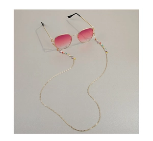 Detail of colorful beads on gold chain with pink gradient sunglasses on gray surface