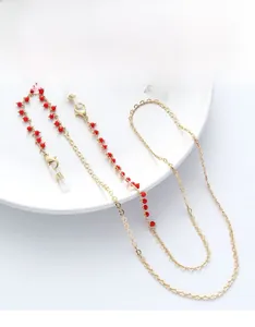 Detail of gold chain glasses strap with red beads on a minimalist white plate
