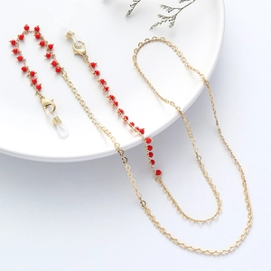 Golden multi-use chain with red beads for glasses and masks on a white ceramic plate