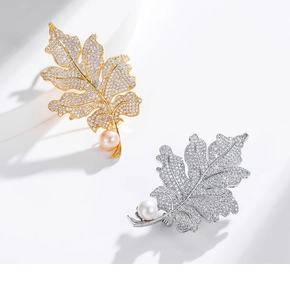 Makro-Detail von gold- und silbernen Blattbroschen mit Zirkon-Pavé und einer Perle