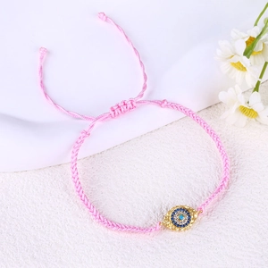 Detail of pink hand-woven Evil Eye bracelet with gold charm and white daisy decor