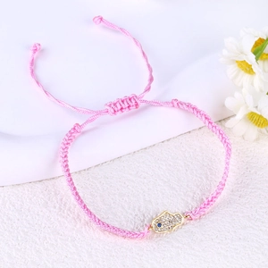 Detail of pink woven bracelet with gold Hamsa hand charm and blue stone inlay