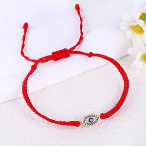 Detailed close-up of a red woven rope bracelet with a gold-plated evil eye charm inlay