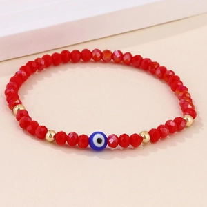 Détail du bracelet artisanal avec perles rouges facettées et breloque œil bleu