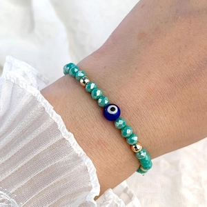Détail du bracelet de perles Evil Eye vertes porté avec des poignets en dentelle