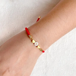 Detalle de pulsera trenzada roja con corazón dorado y cuenta letra K en la muñeca