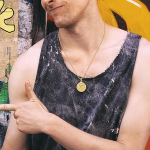 Macro detail of gold coin pendant with Gemini symbol on a male model with street style background