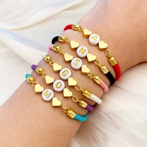Detalle de pulseras de cordón trenzado con dijes de corazón dorados y letras