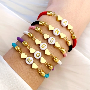 Detalle de pulseras trenzadas ajustables con dijes de corazón y cuentas de letras doradas