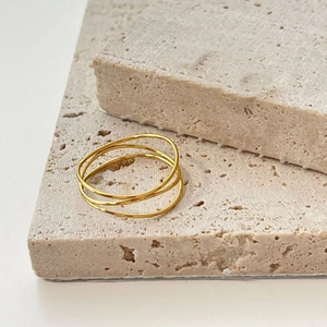 Anillo cruzado de tres capas en acero dorado minimalista sobre superficie de piedra