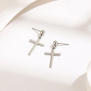 Pendientes de cruz plateada minimalista con tachuelas pulidas sobre tela blanca