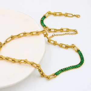 Golden horseshoe U-link chain necklace with green zircon inlay on a white plate