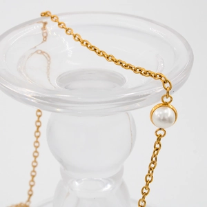Detail einer goldenen O-Kette mit einem glänzenden runden weißen Perlenanhänger