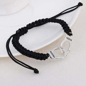 Detail of hand-woven black rope bracelet featuring silver freedom handcuff charms