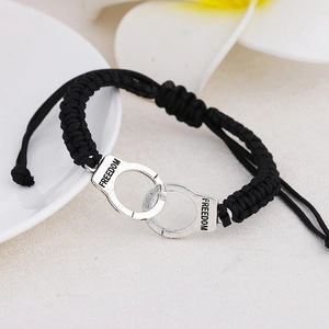 Detail of silver handcuffs charm with Freedom engraving on black braided rope bracelet