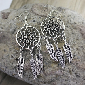 Detalle de pendientes atrapasueños retro con plumas metálicas sobre fondo de piedra rústica