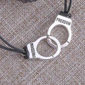 Detail of polished alloy handcuffs with Freedom engraving on black cord bracelet