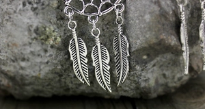 Vista macro de colgante atrapasueños bohemio con plumas y acabado en plata antigua