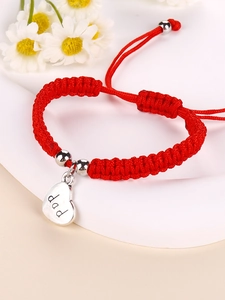 Detail of red braided cord bracelet with silver heart charm engraved with the word dad