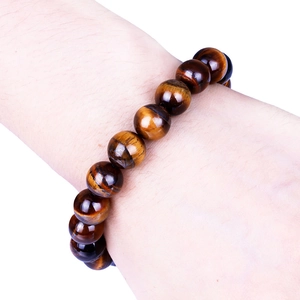 Detail eines Tigerauge-Perlenarmbands mit goldenem Glanz am Handgelenk des Modells