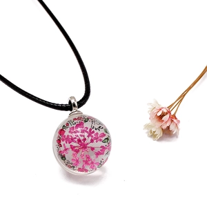 Detailed close-up of a pink real dried flower pendant inside a clear glass sphere