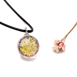 Macro shot of glass ball pendant with yellow dried flower and black cord necklace