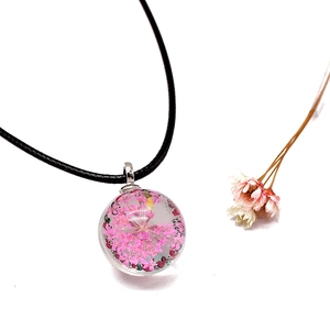 Detail of clear glass globe pendant featuring dried pink flowers with black cord necklace