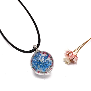 Macro detail of clear glass ball pendant featuring preserved blue and purple dried flowers