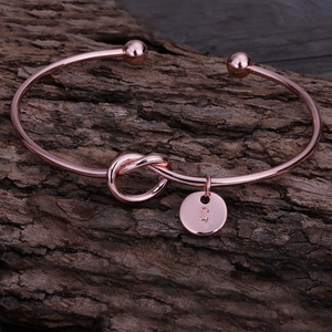 Détail d'un jonc à nœud or rose avec pendentif lettre S sur fond en bois sombre