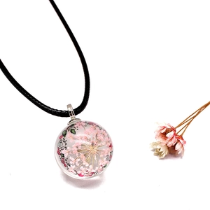 Macro view of handmade glass ball pendant necklace with pink dried flowers and black cord
