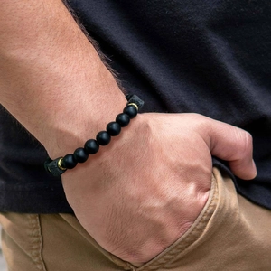 Macro detail of men's matte black beads bracelet with volcanic rock and gold accents