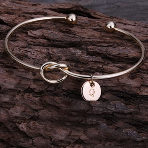Détail d'un bracelet jonc noué doré avec pendentif lettre Q sur un support en bois