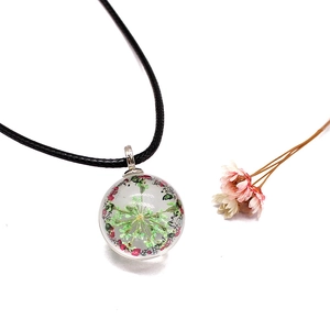 Detail view of handmade glass pendant necklace with real dried lace flowers and black cord