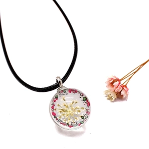 Macro detail of a spherical glass pendant featuring a white dried flower and woven cord