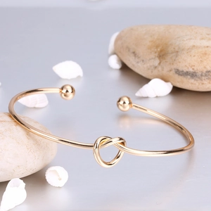 Detail of gold heart knot open cuff bracelet with pebble and shell beach scenery