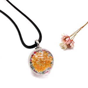 Detailed macro view of yellow dried flower sealed inside a clear glass ball pendant necklace