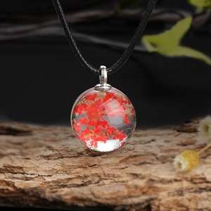 Detail shot of a clear glass sphere necklace with red dried flowers on a rustic wood bark