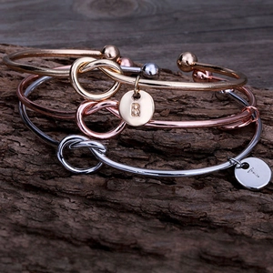 Détail de trois bracelets noués en or, or rose et argent avec breloques alphabétiques
