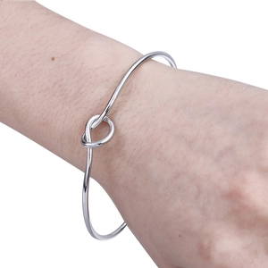 Close-up of a silver knot bangle on a wrist, showcasing the minimalist love knot design