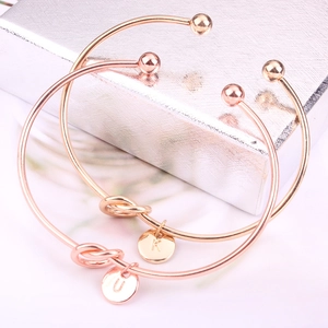 Détail de deux joncs en or rose avec nœuds et pendentifs personnalisés lettres K et U