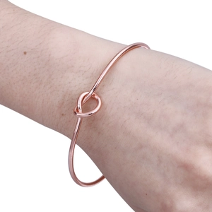 Minimalist rose gold knotted open cuff bracelet shown worn on a female wrist