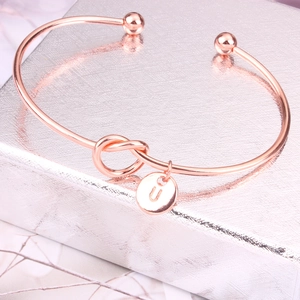 Détail du bracelet jonc nœud en or rose avec un pendentif rond gravé de la lettre U
