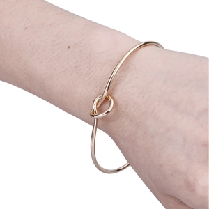 Detailed close-up of a gold knotted open bangle on a woman's wrist in natural light