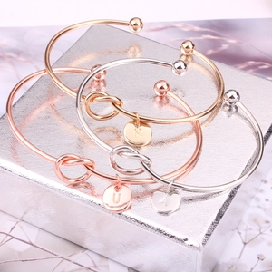 Gros plan de bracelets joncs à nœuds en or, or rose et argent avec breloques de lettres